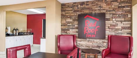 A Red Roof Inn dining area with a brick wall, red leather chairs, a wooden table, and a kitchen in the background.