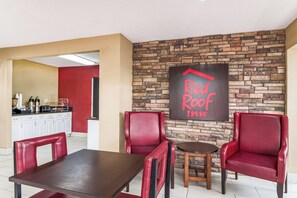 A Red Roof Inn dining area with a brick wall, red leather chairs, a wooden table, and a kitchen in the background. - Red Roof Inn Acworth - Emerson/ LakePoint South (Acworth)