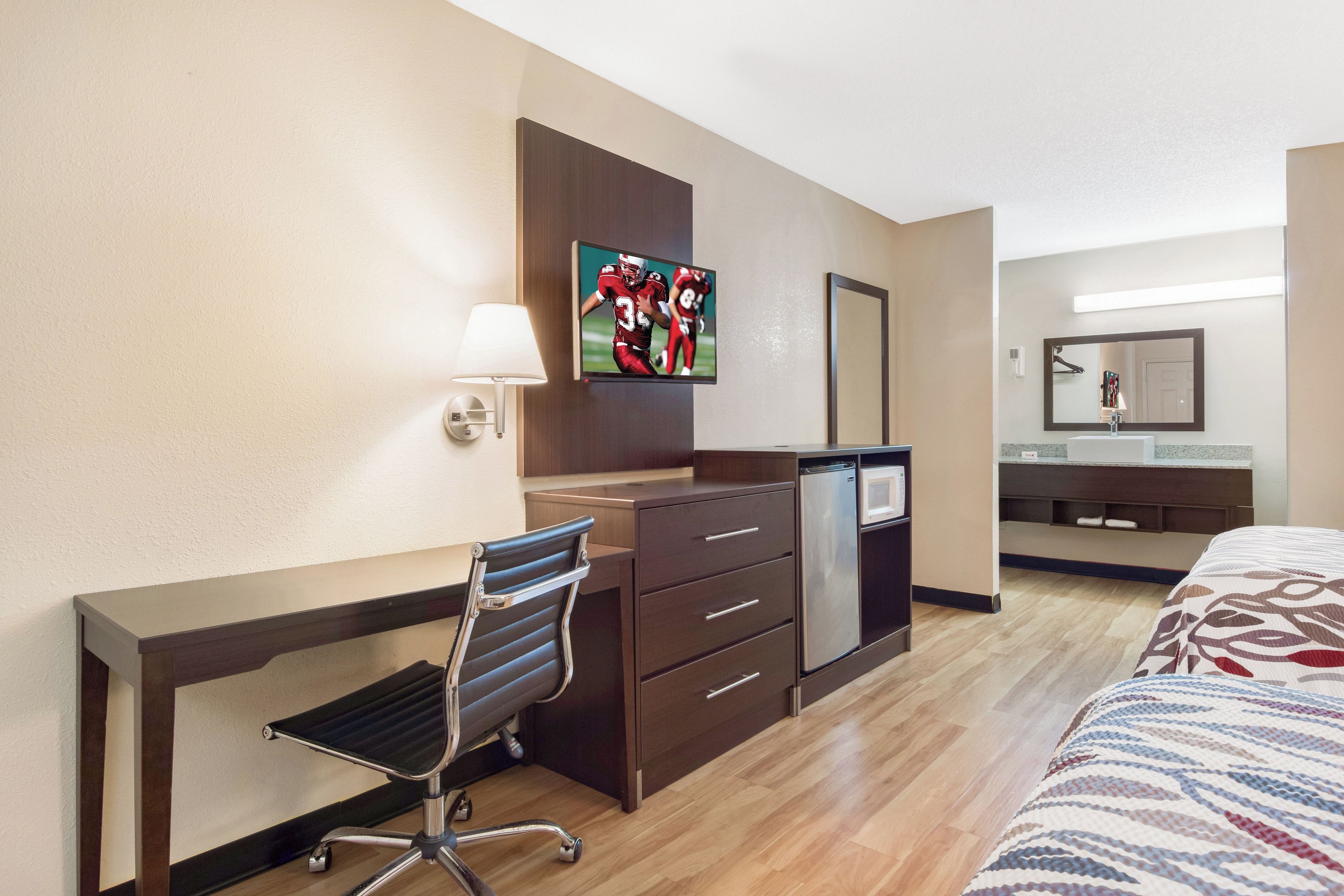 Een hotelkamer met een bureau, stoel, bed, televisie en een spiegel.