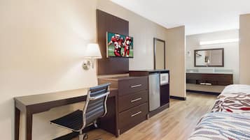 Een hotelkamer met een bureau, stoel, bed, televisie en een spiegel.