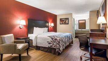 A hotel room with a bed, two chairs, a desk, a mirror, and a bathroom visible in the background.