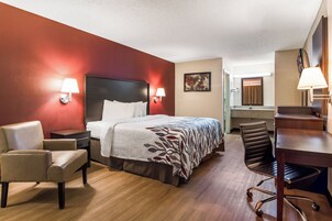 Habitación de hotel con cama, dos sillas, escritorio, espejo y baño visible al fondo.