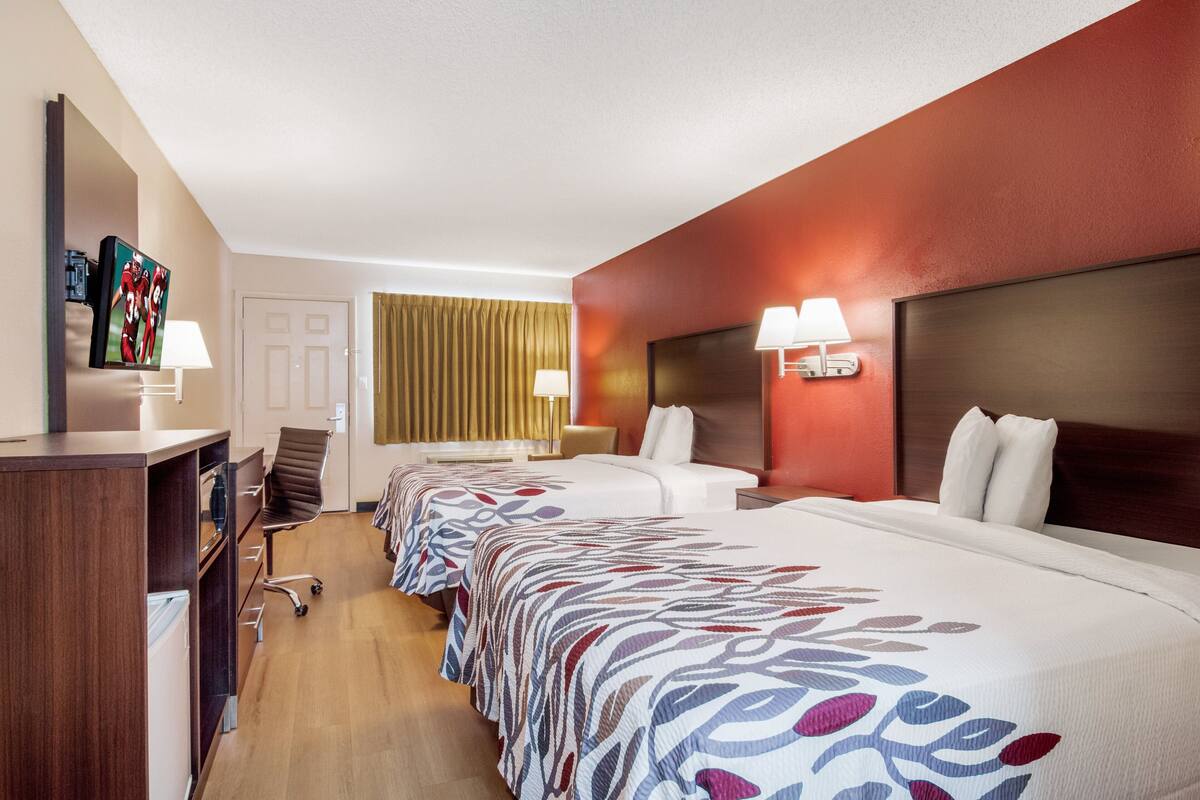 A hotel room with two beds, a desk, a chair, and a TV.
