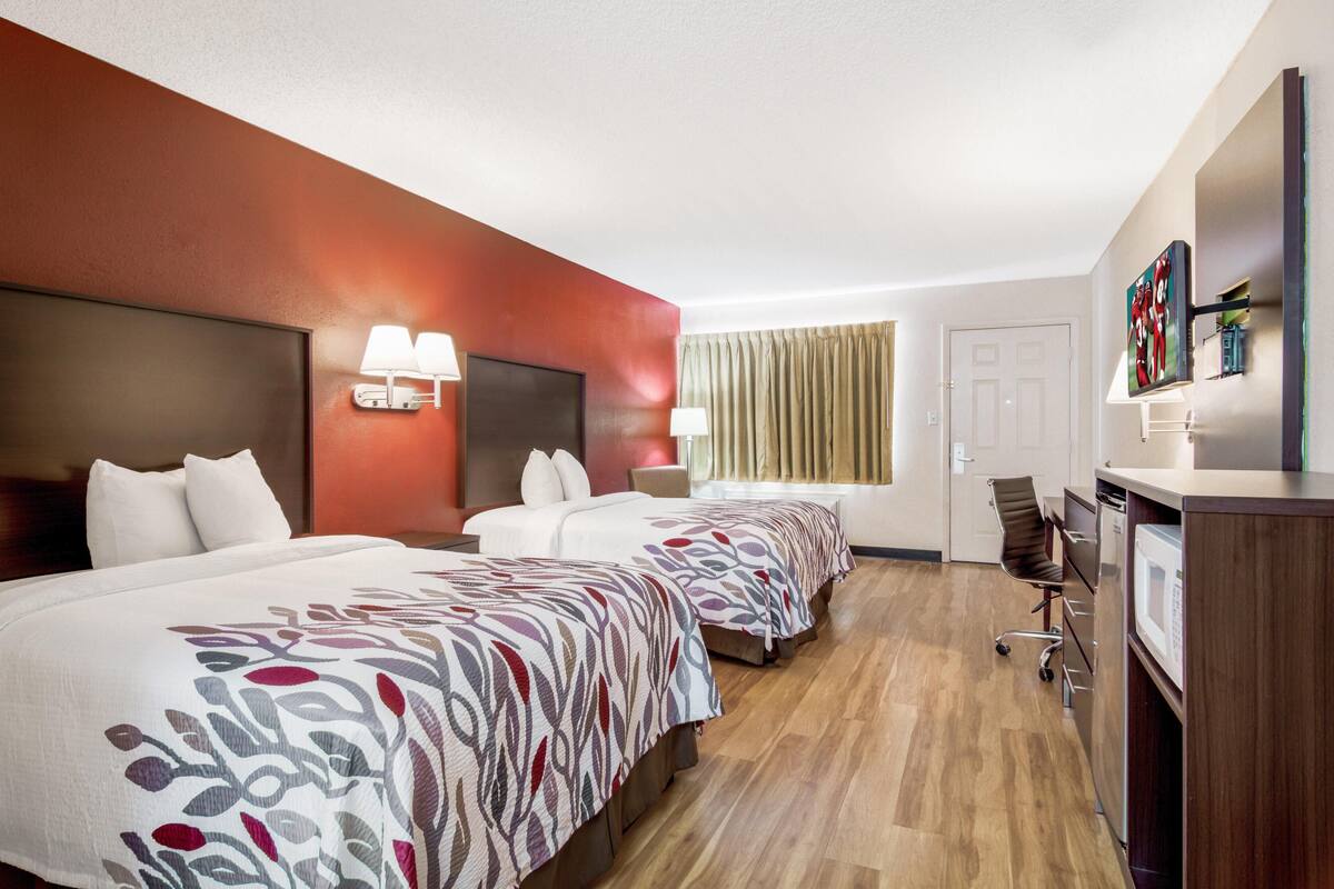 A hotel room with two beds, a desk with a microwave, and a TV.