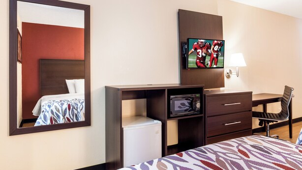 Ein Hotelzimmer mit Bett, Schreibtisch mit Stuhl, Fernseher, Mikrowelle und Spiegel.
