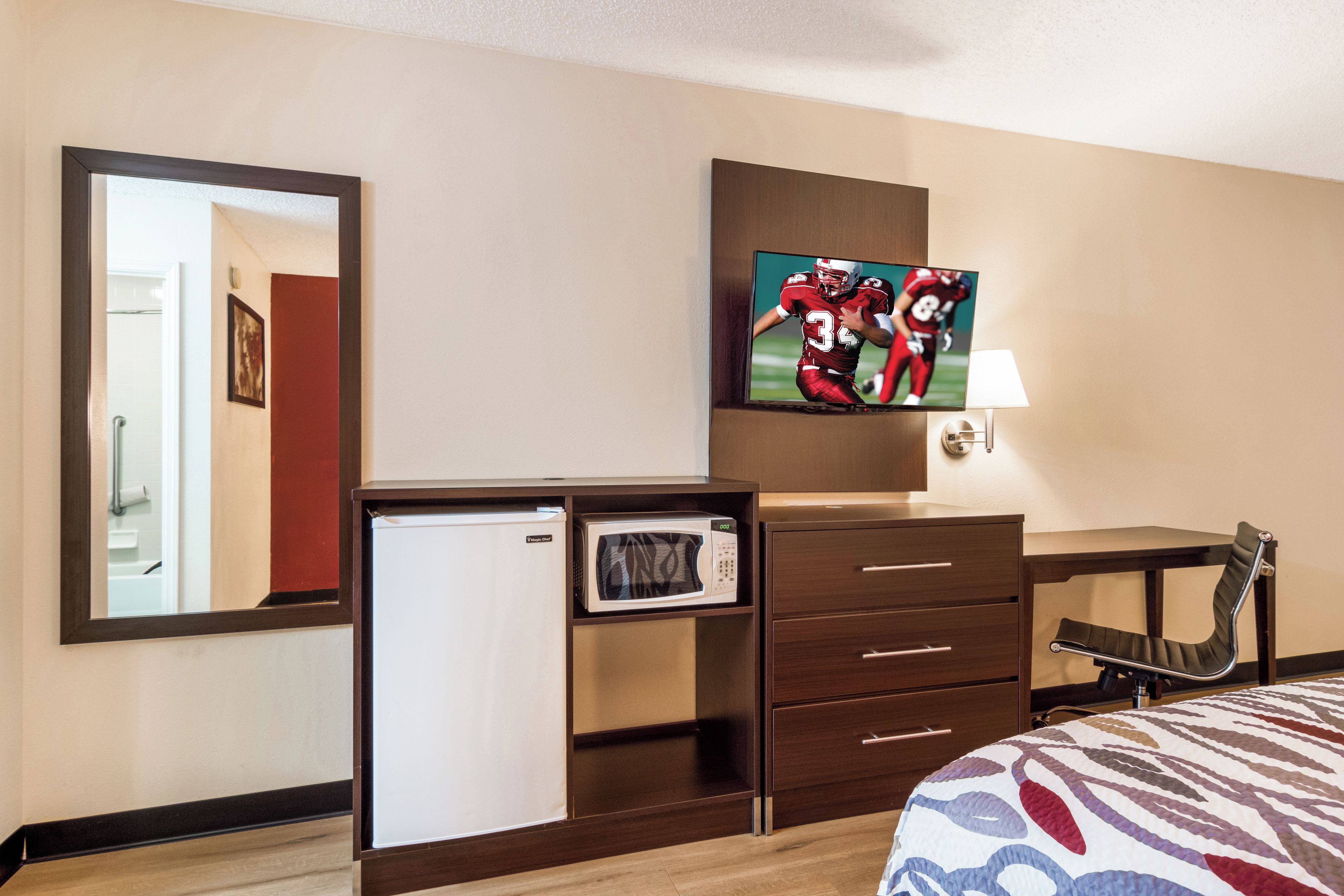 Una habitación de hotel con una cama, un escritorio con televisor, un refrigerador y una silla.