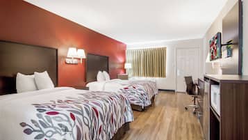 Habitación de hotel con dos camas, un escritorio, una silla, un televisor y una ventana con cortinas.