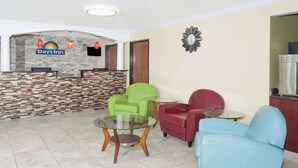 Zona de recepción con el letrero de Days Inn, un mostrador de recepción, un reloj y un área de descanso con sillas verdes y rojas.