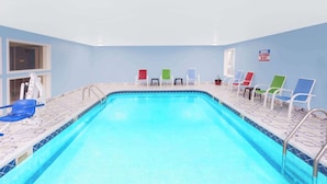 Una piscina interior con suelo y paredes de baldosas azules, rodeada de sillones blancos y de colores.