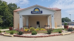 Un hotel Days Inn con vestíbulo techado, mobiliario exterior y macizos de flores.