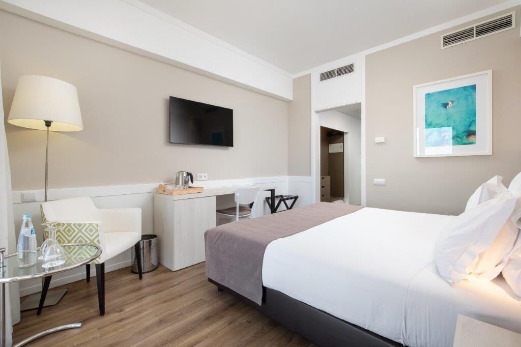 Habitación de hotel con cama, escritorio, silla, lámpara y televisor.