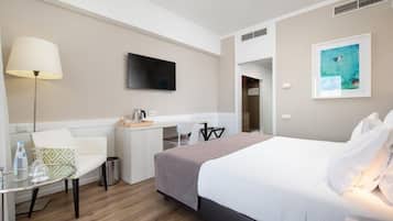 Habitación de hotel con cama, escritorio, silla, lámpara y televisor.