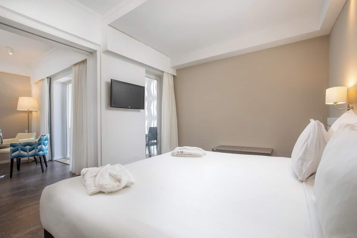 Camera d'albergo con un letto grande, una televisione a schermo piatto fissata al muro, una scrivania con una sedia e una finestra con tende.