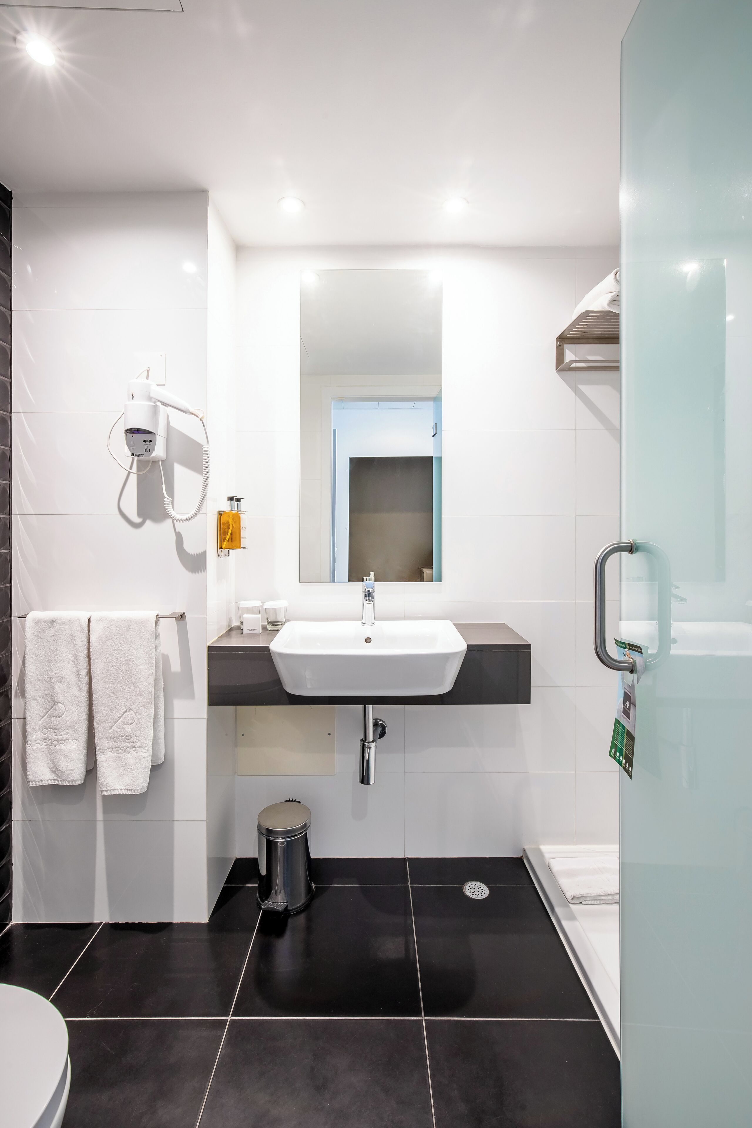 Un baño moderno con un lavabo blanco, un espejo, un perchero y un cubo de basura.