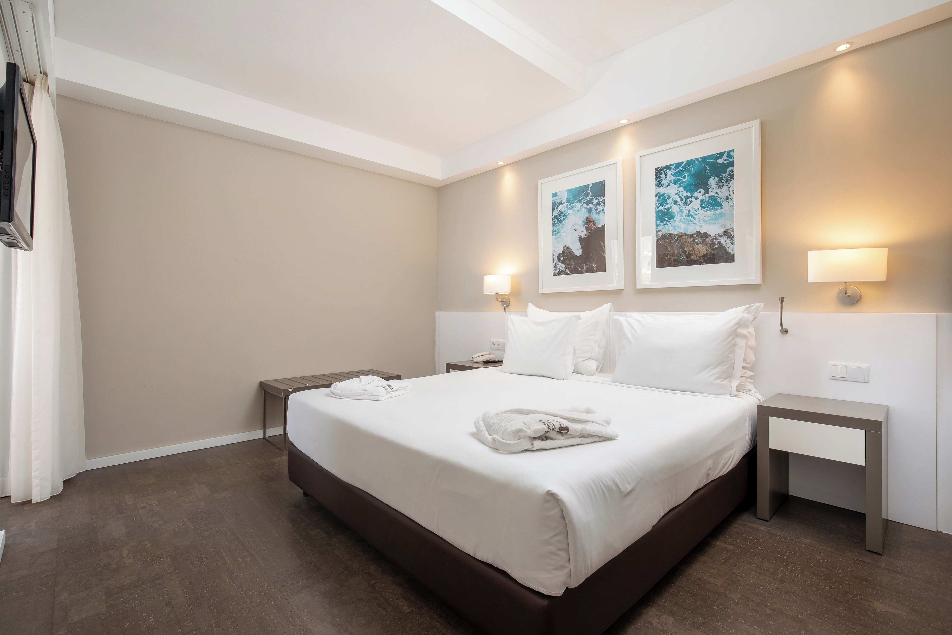 Une chambre d’hôtel avec un grand lit, deux tables de chevet et des œuvres d’art accrochées aux murs.