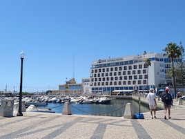 Un puerto deportivo con barcos, un hotel llamado 'EVA SENSES HOTEL' y un cielo azul despejado.