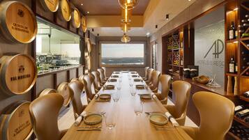 Mesa de jantar comprida posta para uma refeição num restaurante com barris de madeira nas paredes e vista para o mar.