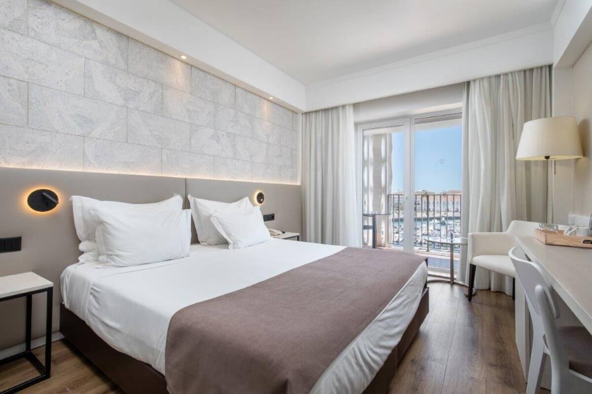 Una camera d'albergo moderna con un letto grande, una scrivania e un balcone con vista sulla città.