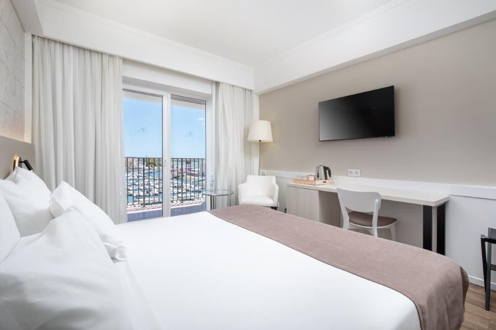 Een hotelkamer met een bed, een bureau, een stoel, een televisie en een balkon met uitzicht.