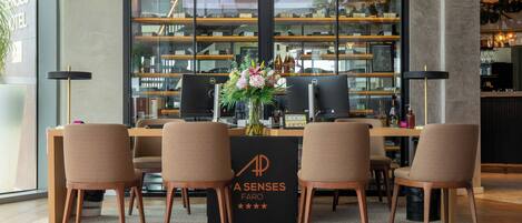 A hotel reception area with a reception desk, four chairs, a black sign with 'A SENSES FARO' and five stars, and a large window displaying shelves with various items.