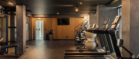 Un gimnasio con cintas de correr, bicicletas estáticas y una televisión instalada en la pared.