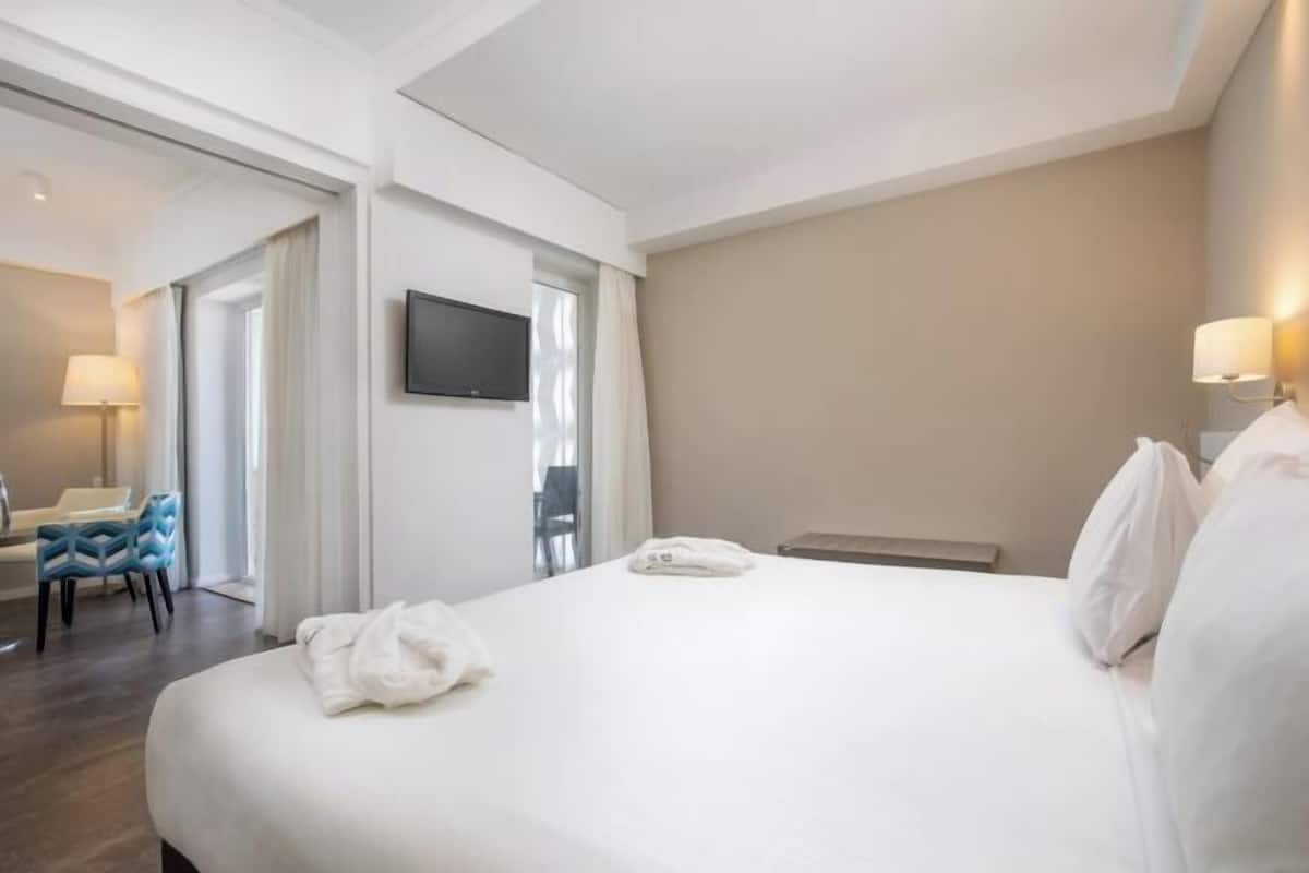 Una camera d'albergo con un letto, una TV a muro, una scrivania con una lampada e una sedia.