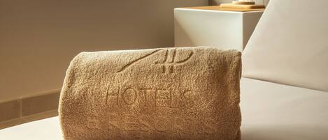 A hotel room with a large window, a white sofa, and a towel with embossed text.