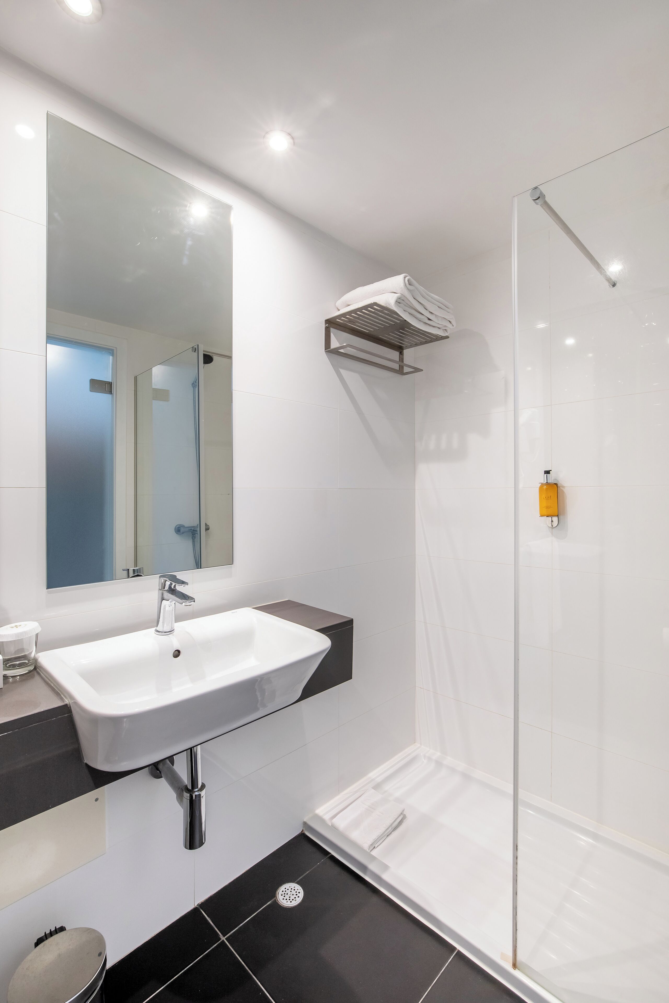 Een moderne badkamer met een witte wastafel, een grote spiegel en een douchecabine van glas.