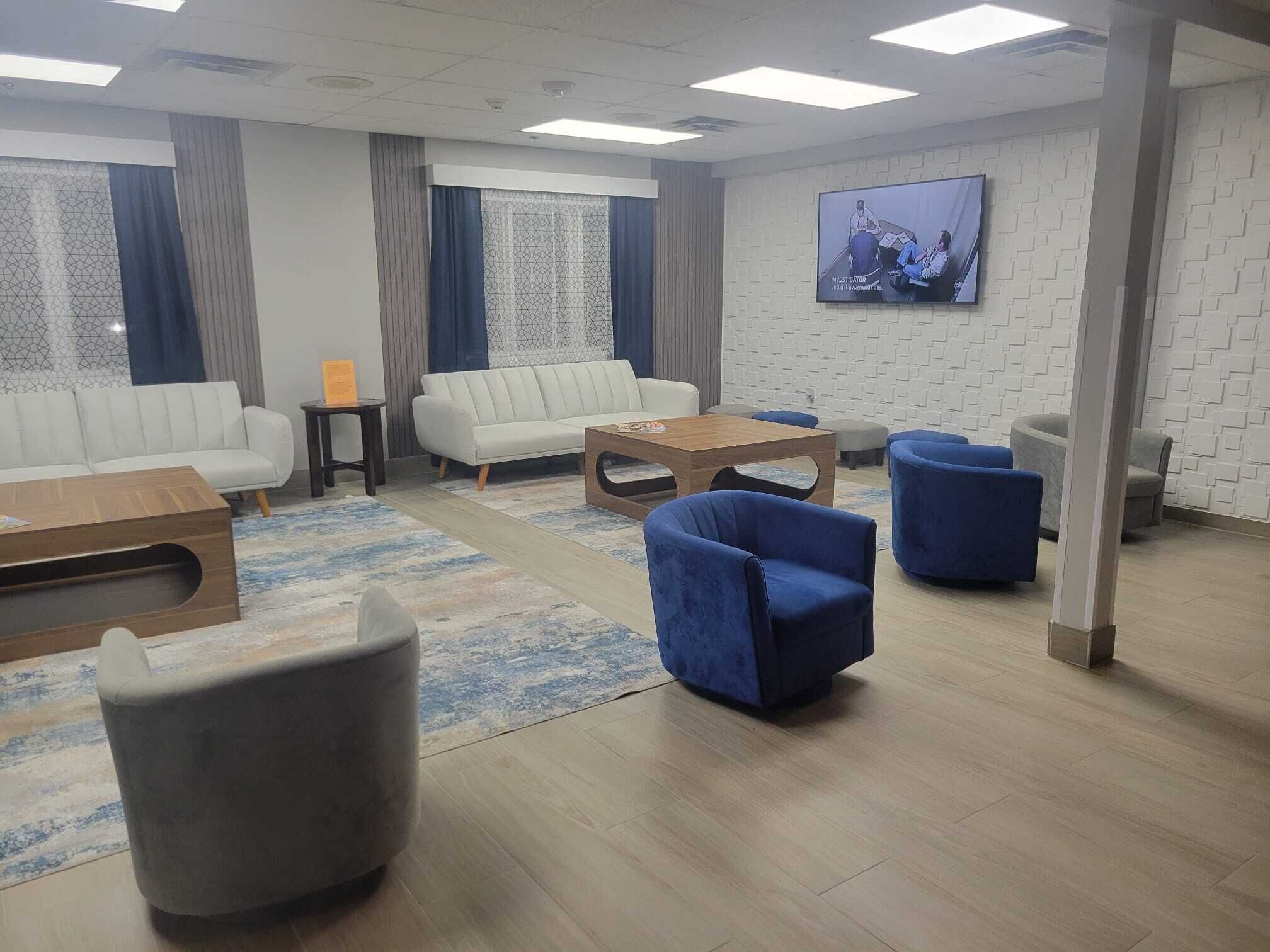 Un área de estar moderna con sofás, sillones, una mesa de centro y un televisor montado en la pared.