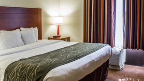 Ein Hotelzimmer mit einem großen Bett, einer Nachttischlampe, einem Heizkörper und einem Fenster mit gestreiften Vorhängen.