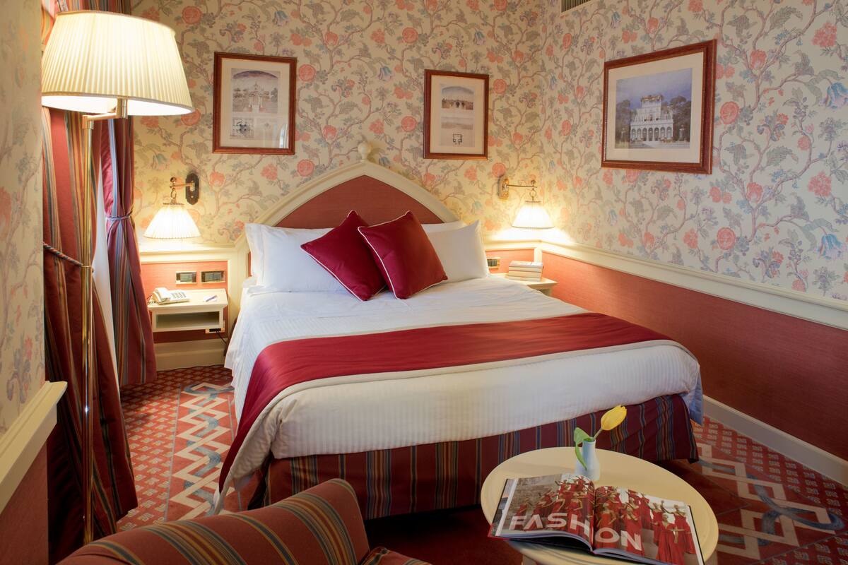 Ein Hotelzimmer mit einem großen Bett, zwei Nachttischlampen, einem Nachttisch, einem Sessel und einer Zeitschrift auf dem Tisch.