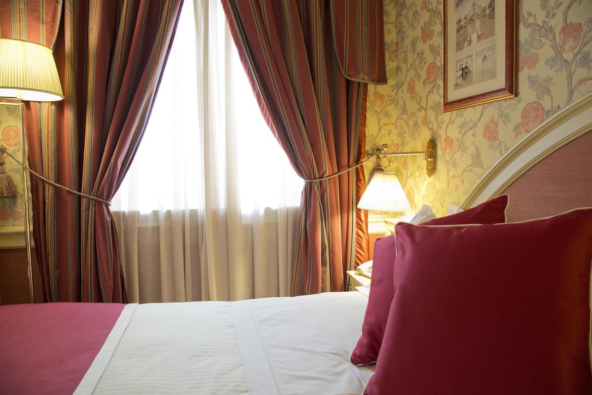 Ein Hotelzimmer mit Bett, Vorhängen, einer Lampe und Blumenwallpaper.