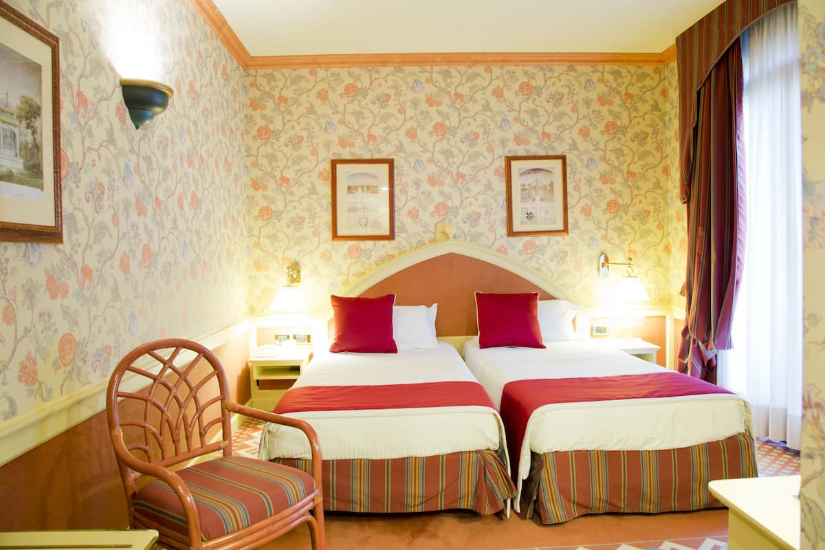 Ein Hotelzimmer mit zwei Betten, einem Holzhocker und blumigem Wandpapier.