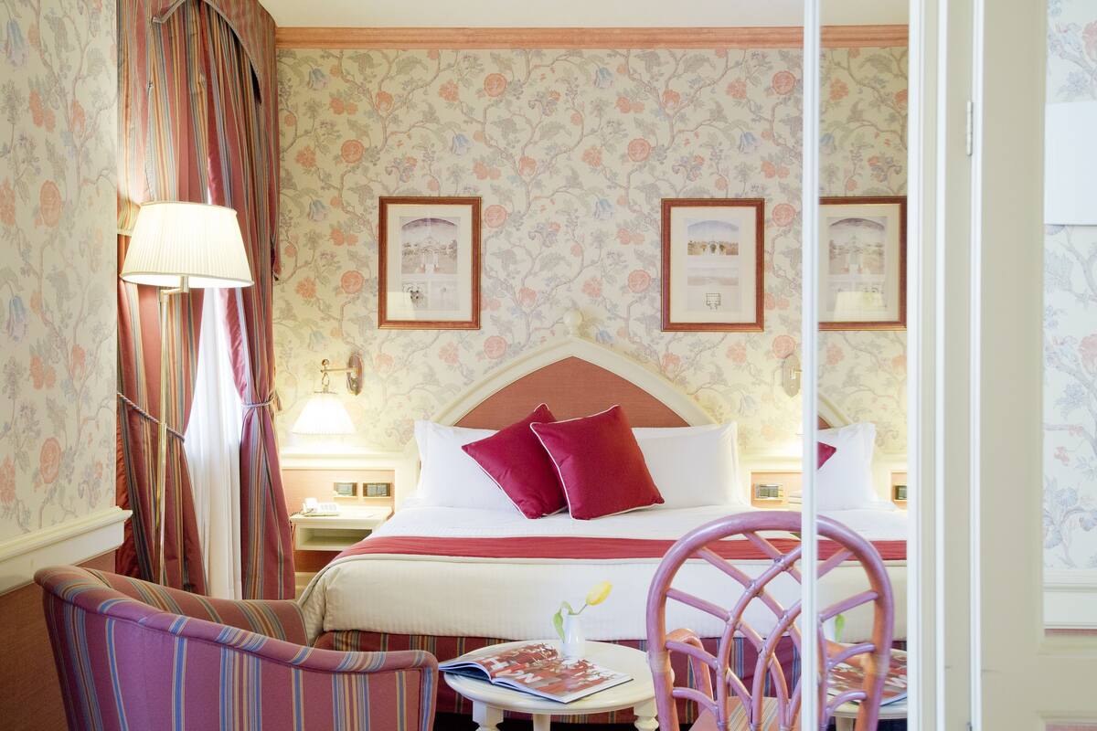 Ein Hotelzimmer mit Bett, Sessel, Tisch und Lampe.