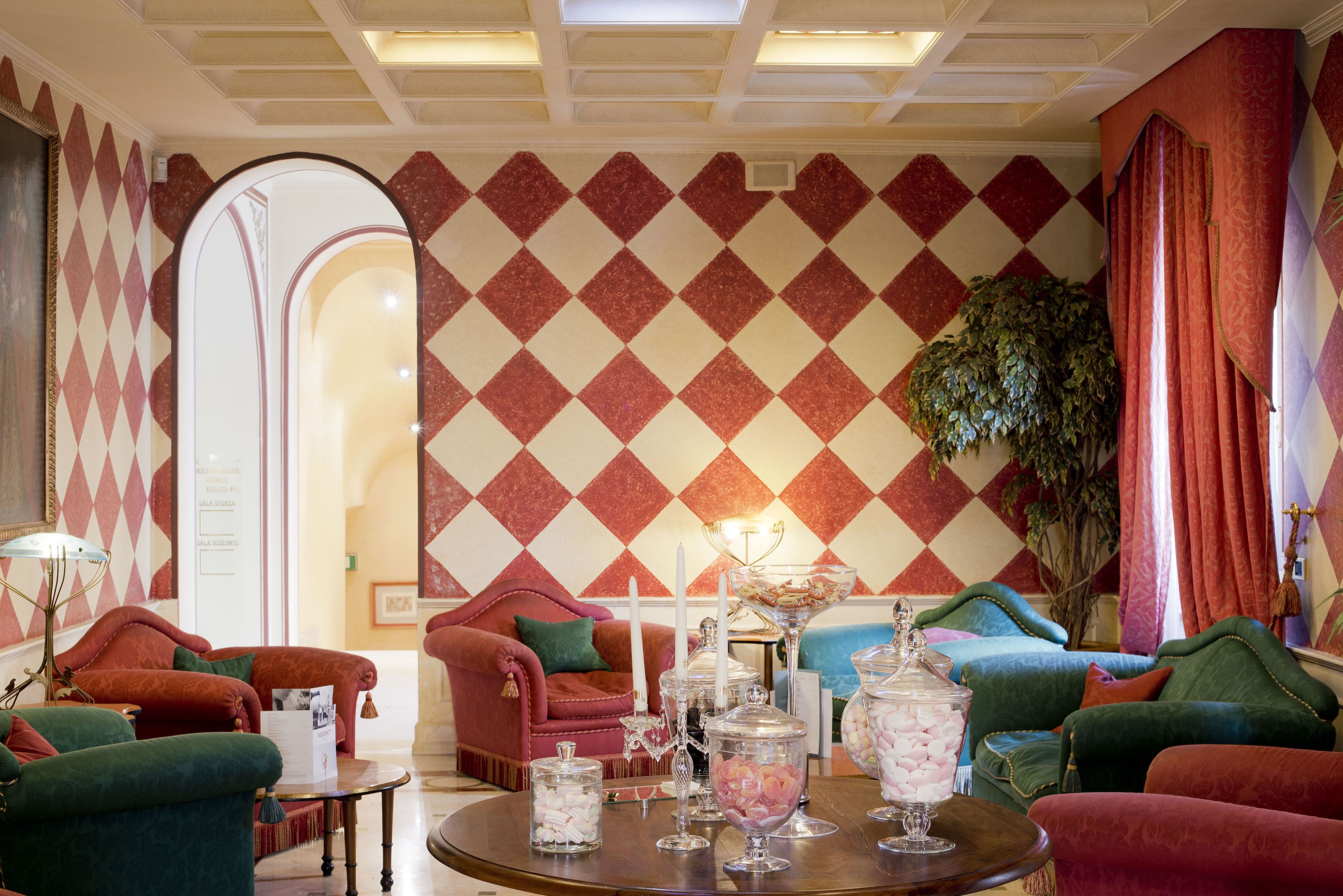 Eine Lobby mit karierter Wand, bequemen Sitzgelegenheiten, einem Kronleuchter und einer großen Pflanze.