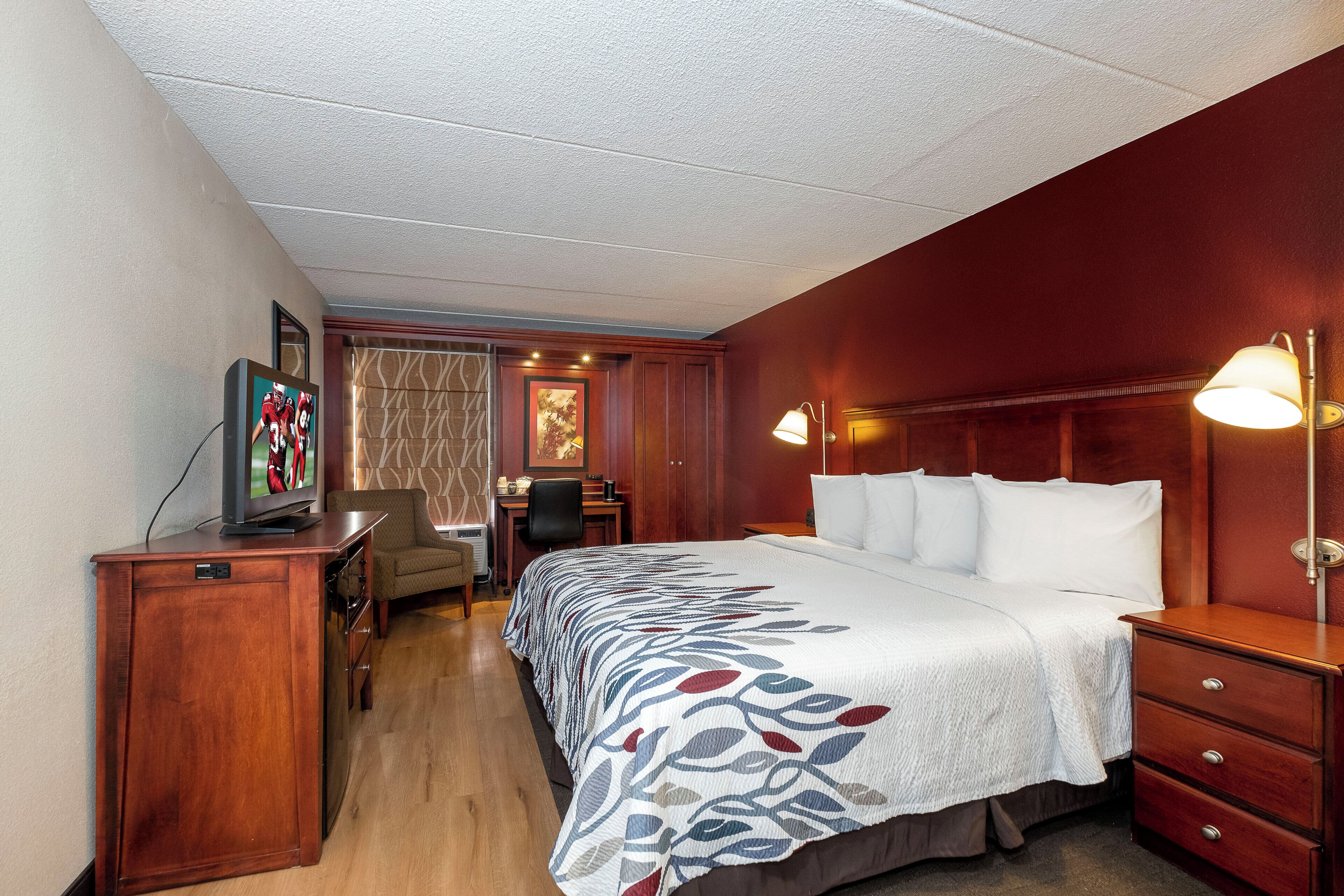 Una habitación de hotel con cama, escritorio, silla y televisor sobre un aparador de madera.