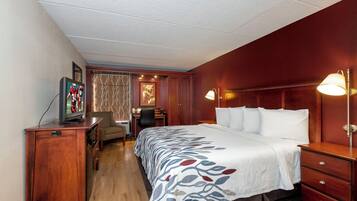 Una habitación de hotel con cama, escritorio, silla y televisor sobre un aparador de madera.