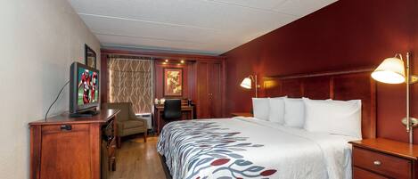 Una habitación de hotel con cama, escritorio, silla y televisor sobre un aparador de madera.