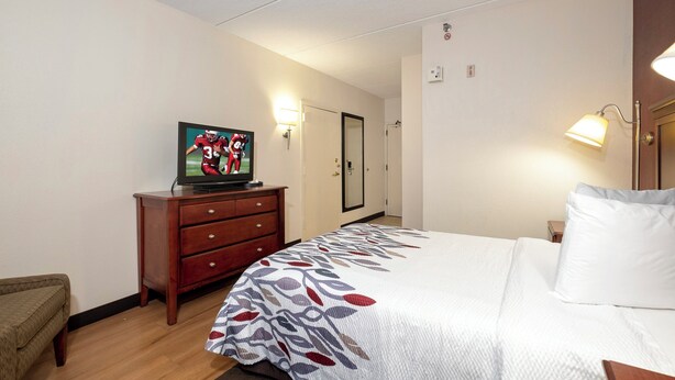 A hotel room with a bed, a dresser, a television, and a door.