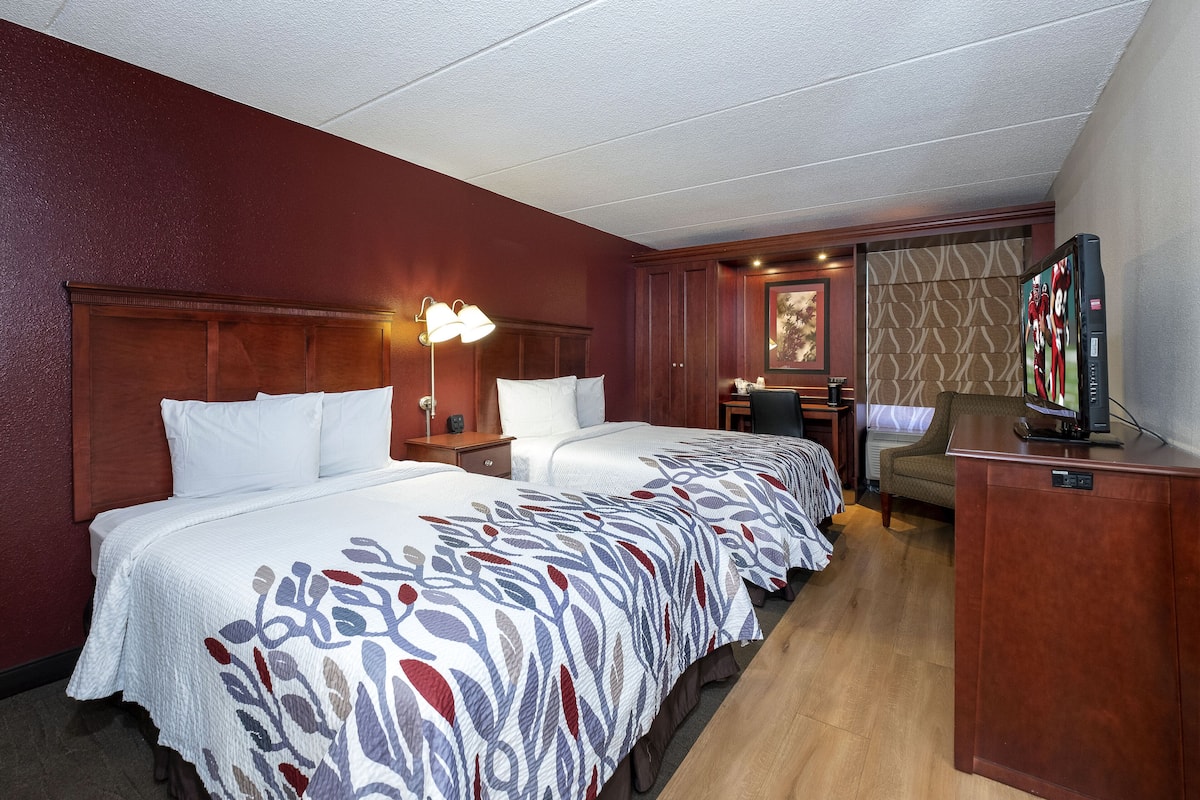 A hotel room with two beds, a desk, a television, and a chair.