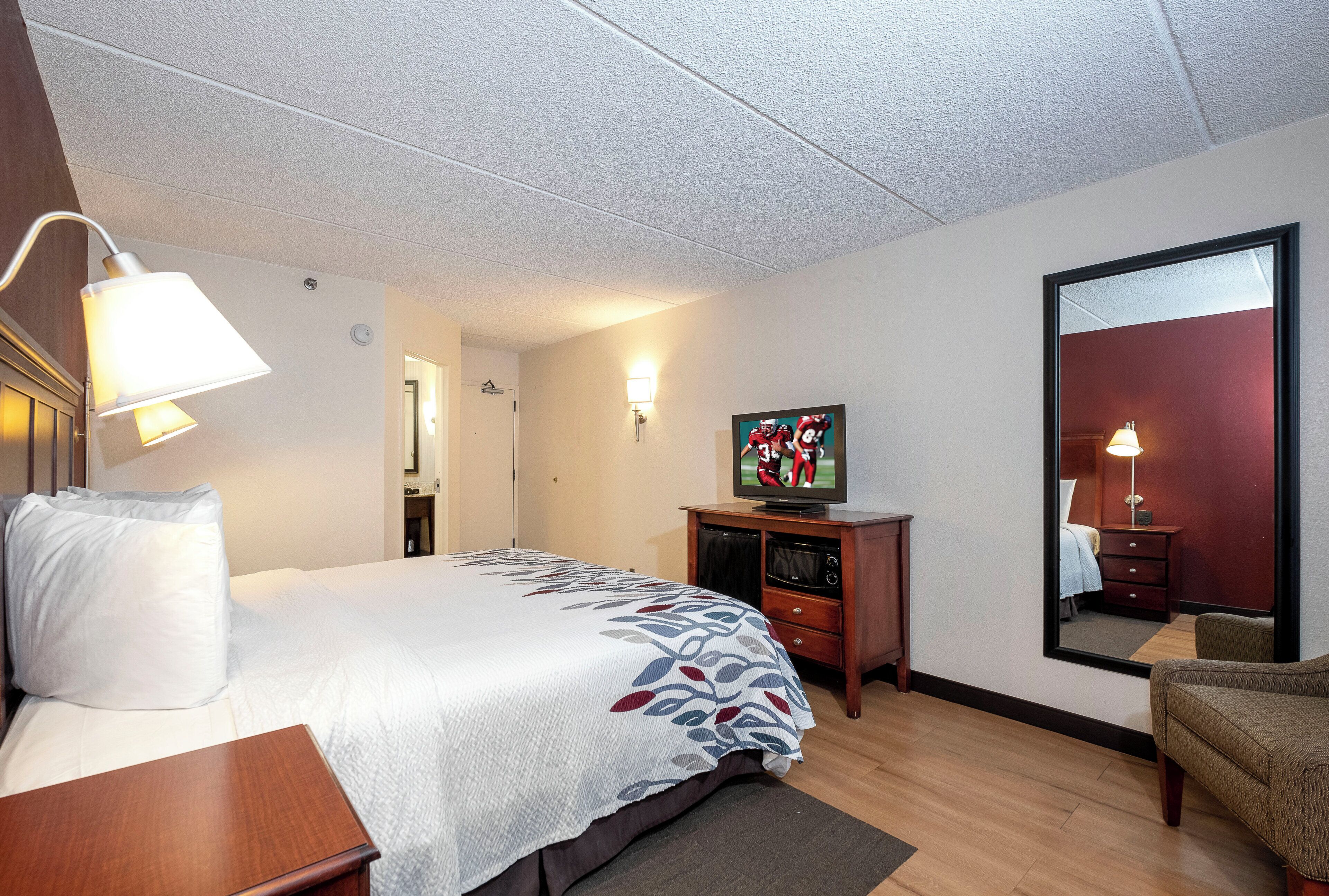 A hotel room with a bed, a television, a desk, and a mirror.
