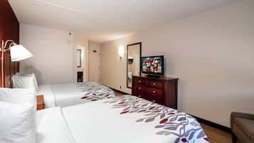 Ein Hotelzimmer mit zwei Betten, einem Fernseher, einem Schminktisch und einem Spiegel.