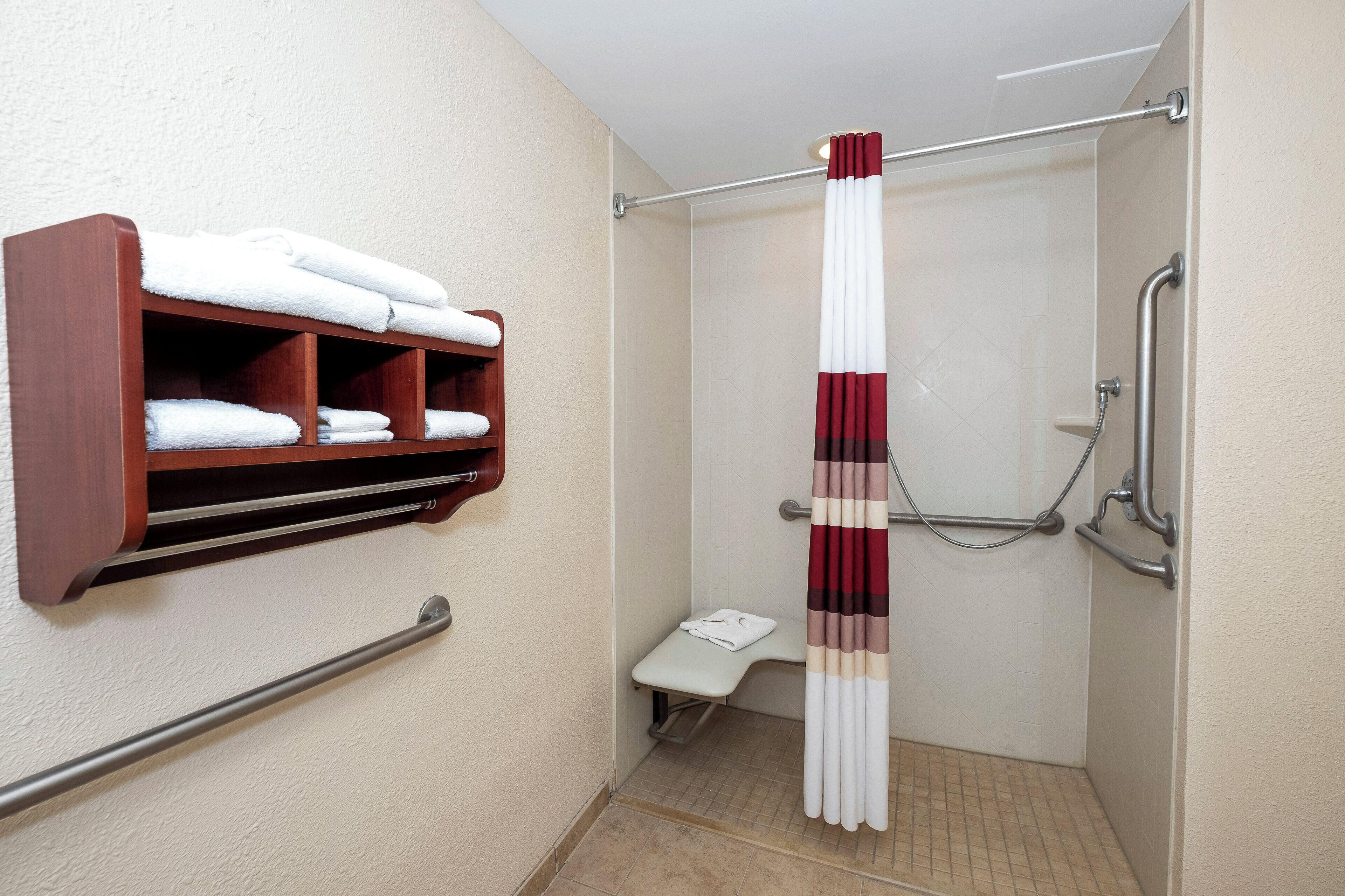 A small, accessible shower area with a grab bar, a shelf with folded towels, and a shower curtain.