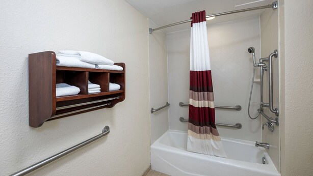 Une salle de bain avec une baignoire blanche, un porte-serviettes en bois sur lequel sont pliées des serviettes, et un rideau de douche.
