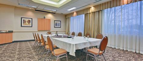 A conference room with a long table, chairs, a carpeted floor, and a view through large windows.