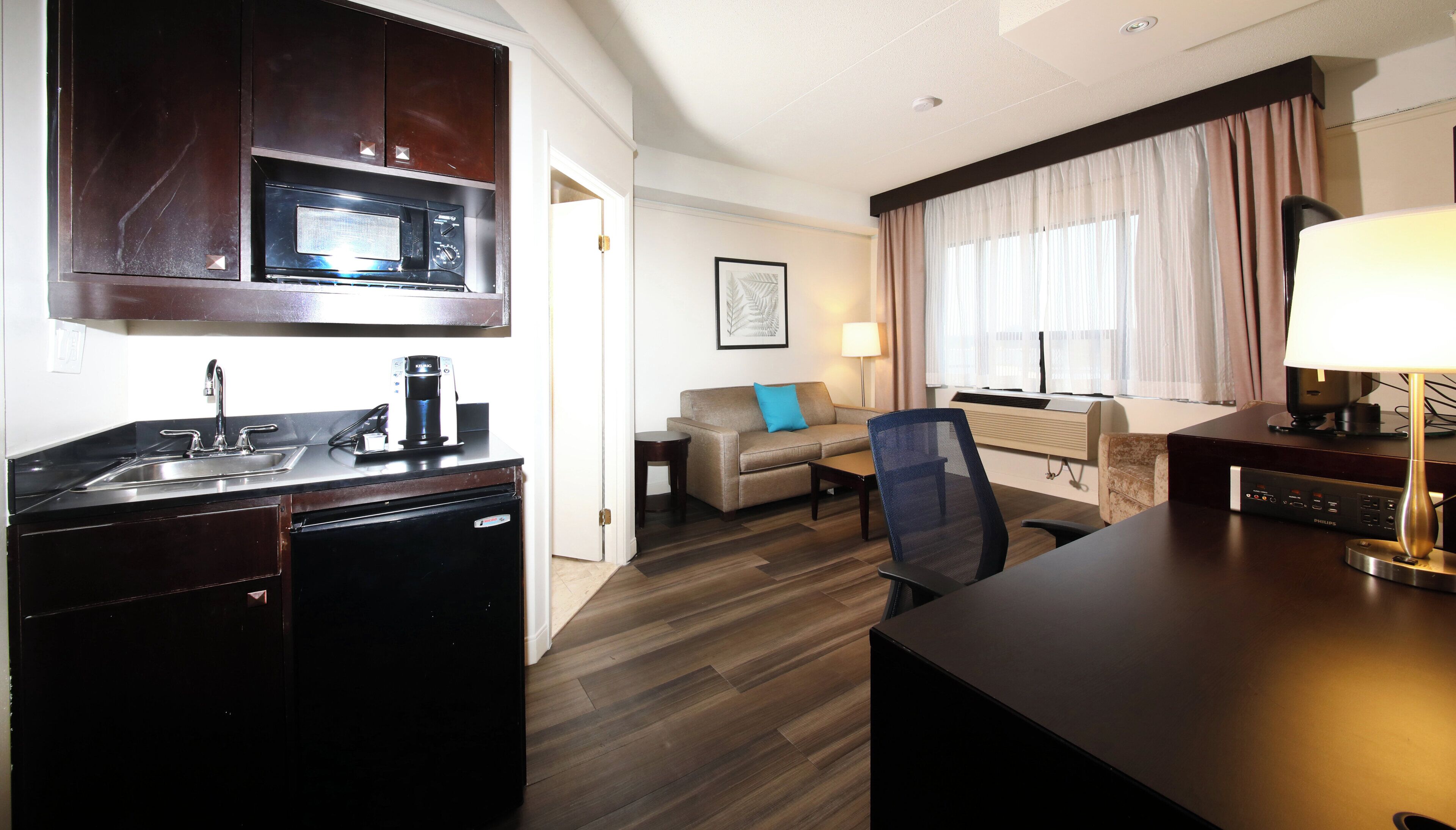 Une chambre d’hôtel compacte comprenant un coin cuisine, un canapé, un bureau et une lampe.