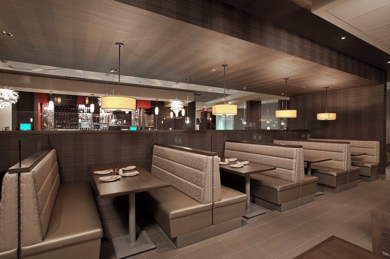 A modern restaurant interior with booth seating, pendant lighting, and a bar area in the background.