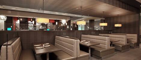 A modern restaurant interior with booth seating, pendant lighting, and a bar area in the background.