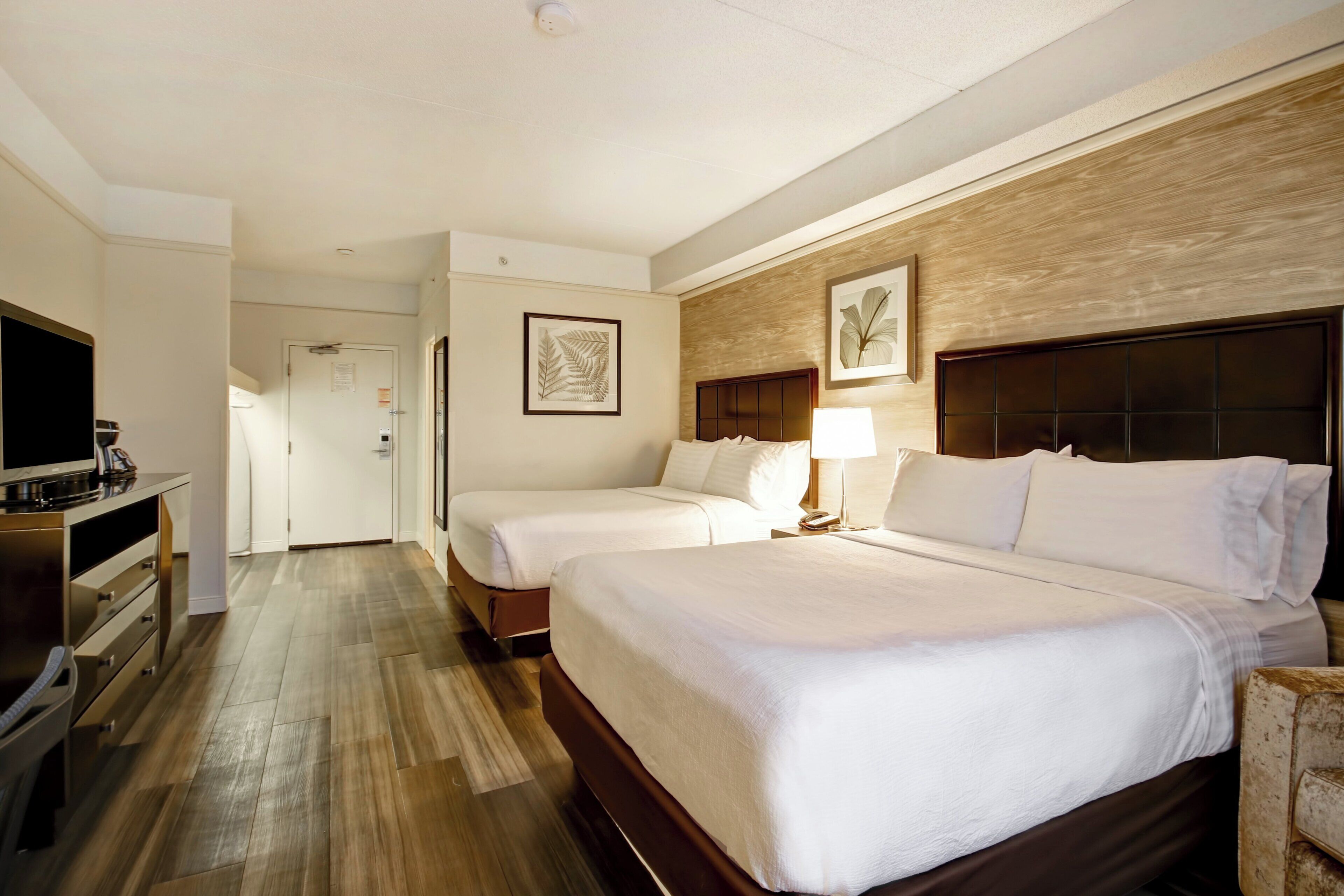 Une chambre d’hôtel avec deux lits, un bureau doté d’un téléviseur à écran plat, un plancher en bois et une œuvre d’art accrochée au mur.