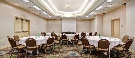 Un salón de conferencias con varias mesas y sillas, una pantalla de proyector y una alfombra estampada.